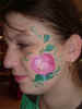 Face Painting: Adult female with cheek painted pink apple framed with vine of green leaves.