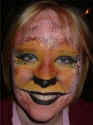 Face Painting: Smiling blonde adult female with painted monkey face in shades of orange, yellow and pink.