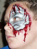 Special Effects: Left hand profile of boy with a metallic silver patch extending from the upper temple to below the cheekbone. Synthetic blood appears to ooze from the edges of the patch, and to drip down the cheek. This gives the impression of there being a metallic cyborg type skeletal structure beneath the natural skin.Casualty simulation of this nature is employed for both practical first aid training and in theatrical makeup. Television, theatre and the film industry use our techniques. For medical training Cool Faces can provide realistic artificial burns, cuts, grazes and other injuries, as required.